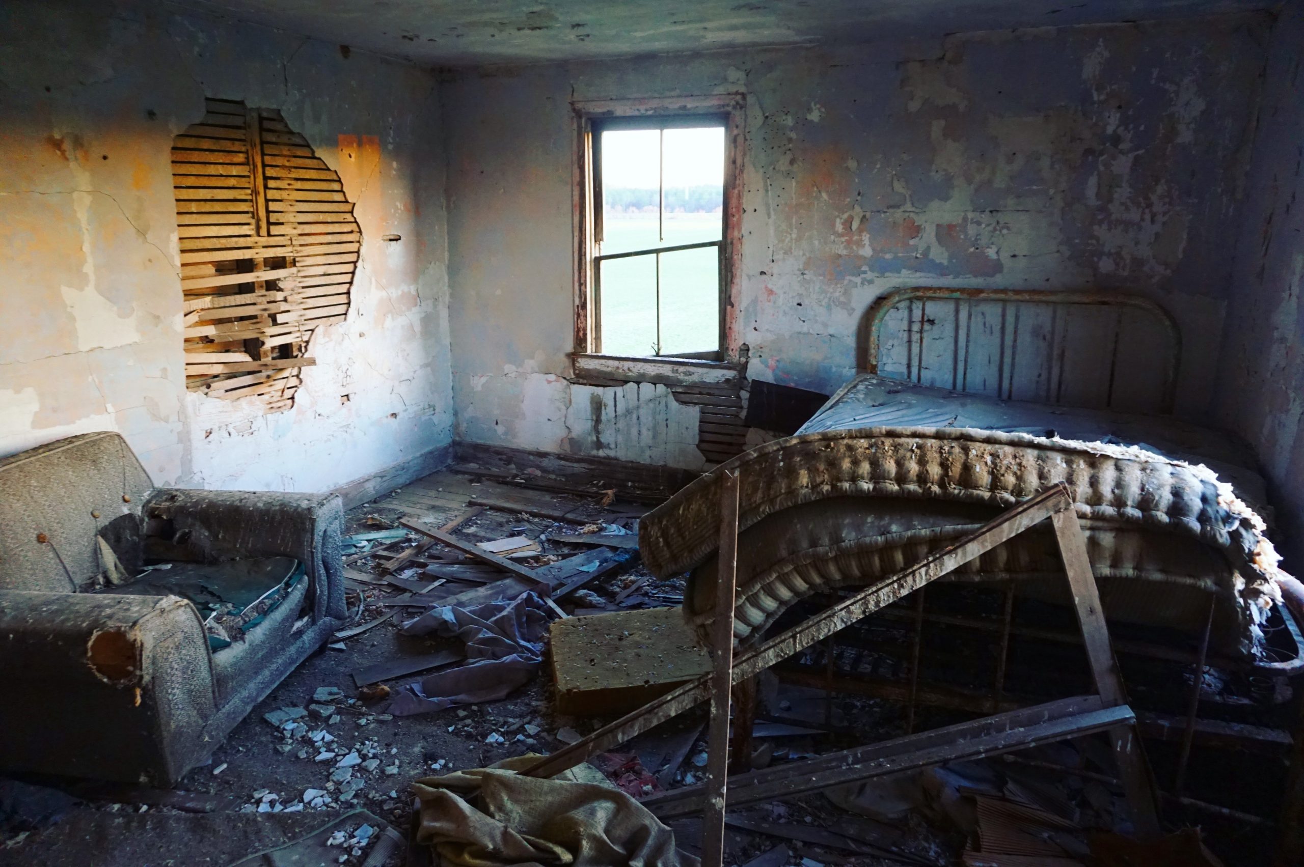 Derelict room with sagging bed and window, exposed timbers, mold